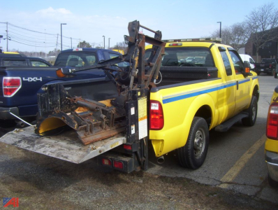 Ford F-250 Super Duty pickup with plow equipment mounted in the bed, yellow service pickup with blue stripe, rear view showing plow attachment