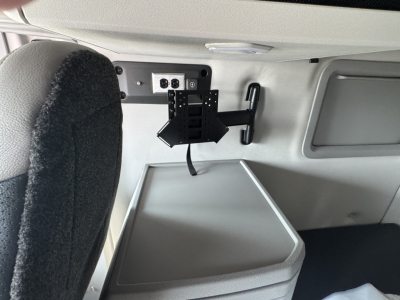 Trailerless? Volvo sleeper cab interior showing a wall-mounted bracket and a small electronic panel with screws and a strap. No visible text aside from a generic harness plate.