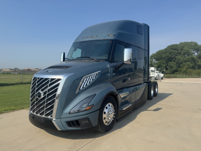 2026 Volvo VNL64T860 in-service sleeper tractor with large front grille, Volvo emblem, chrome mirrors, and aerodynamic cab, parked on pavement.