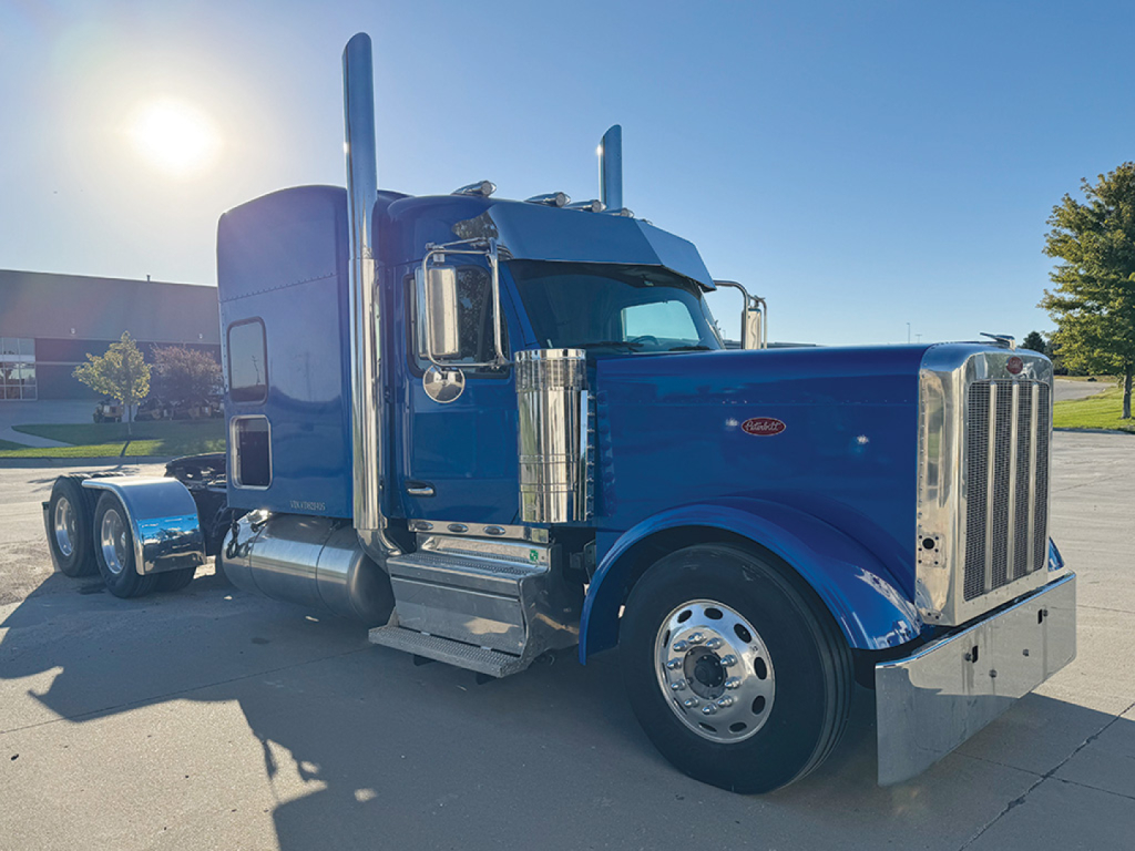 Peterbilt 589 UltraCab extended hood truck in blue, side view showing tall exhaust stacks, chrome grille, and dual rear axles.