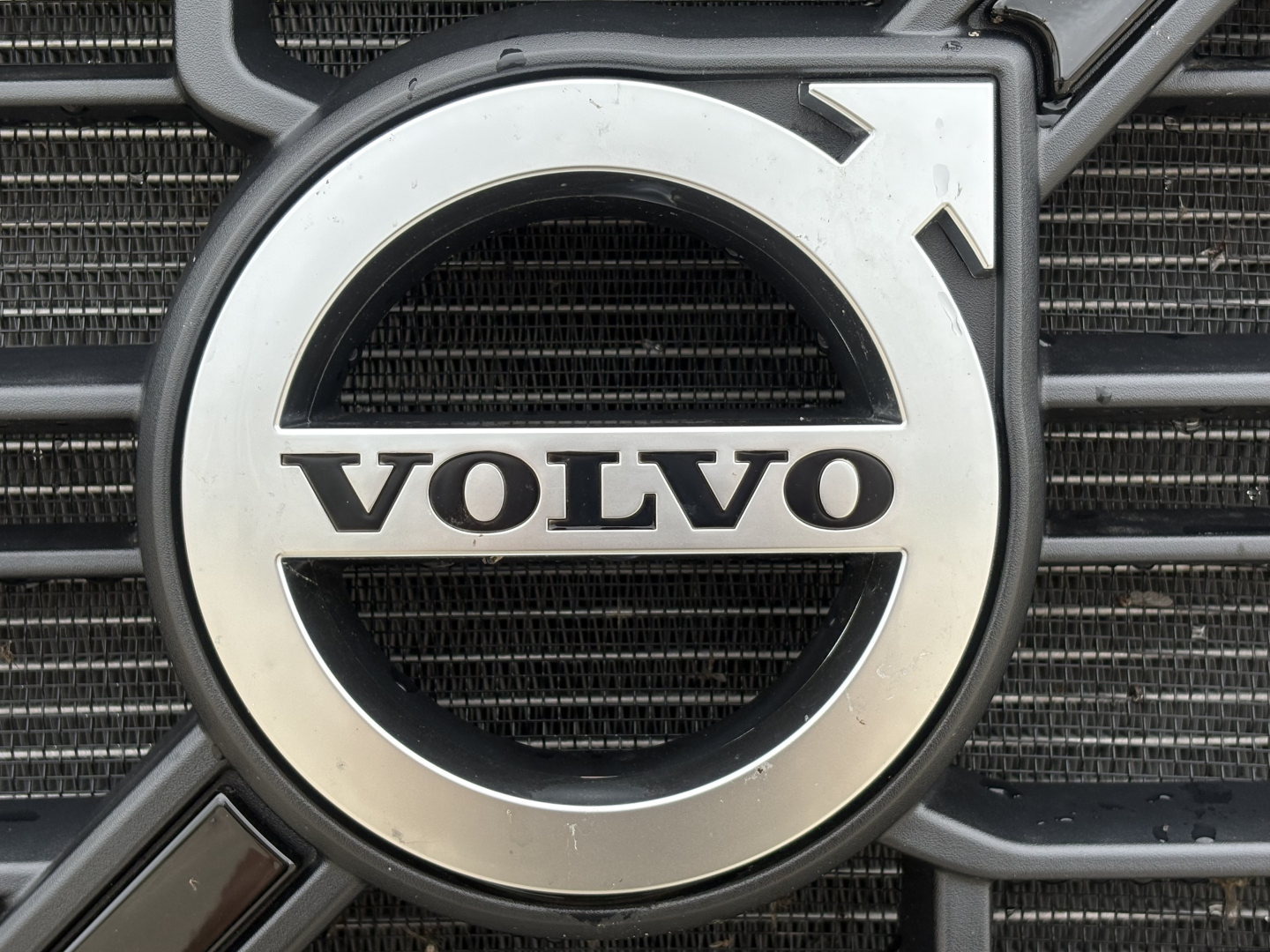Front grille of Volvo truck with Volvo emblem, part of radiator visible.