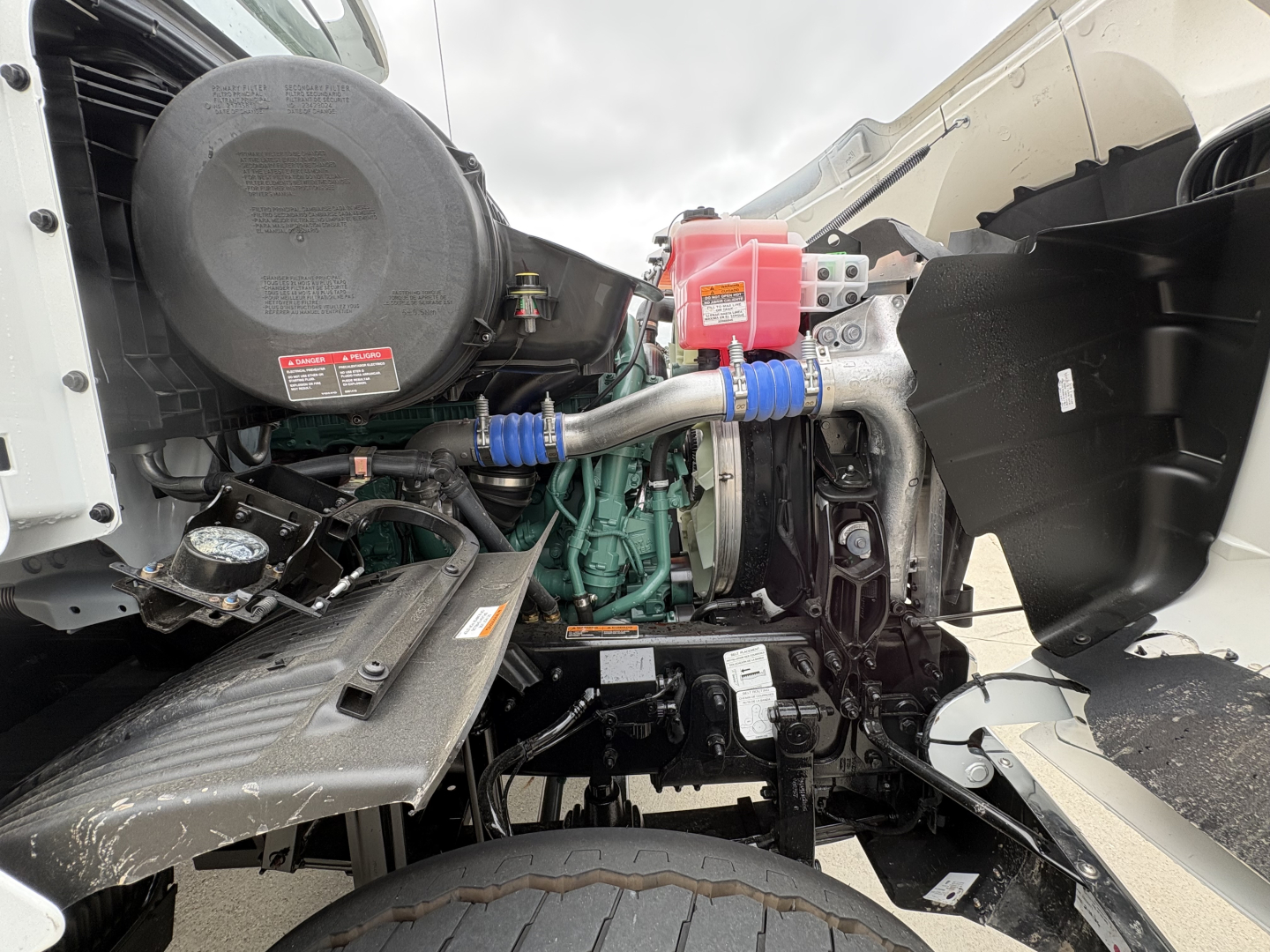 Engine bay of a Volvo VHD84F300 dump truck showing green engine, air intake, red battery box, hoses, belts, and surrounding components.
