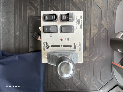 Control panel with switches and indicator lights mounted on a Volvo dump truck floor mat showing buttons labeled ON/OFF, 12V, and two lo/hi range indicators.