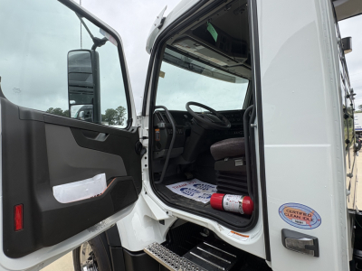 Volvo VHD84F300 dump truck cab interior visible through open door with steering wheel, driver seat, and entry step; certification sticker on door jamb.