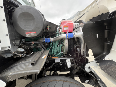 Engine bay of a Volvo VHD84F300 dump truck showing green engine, air intake, red battery box, hoses, belts, and surrounding components.