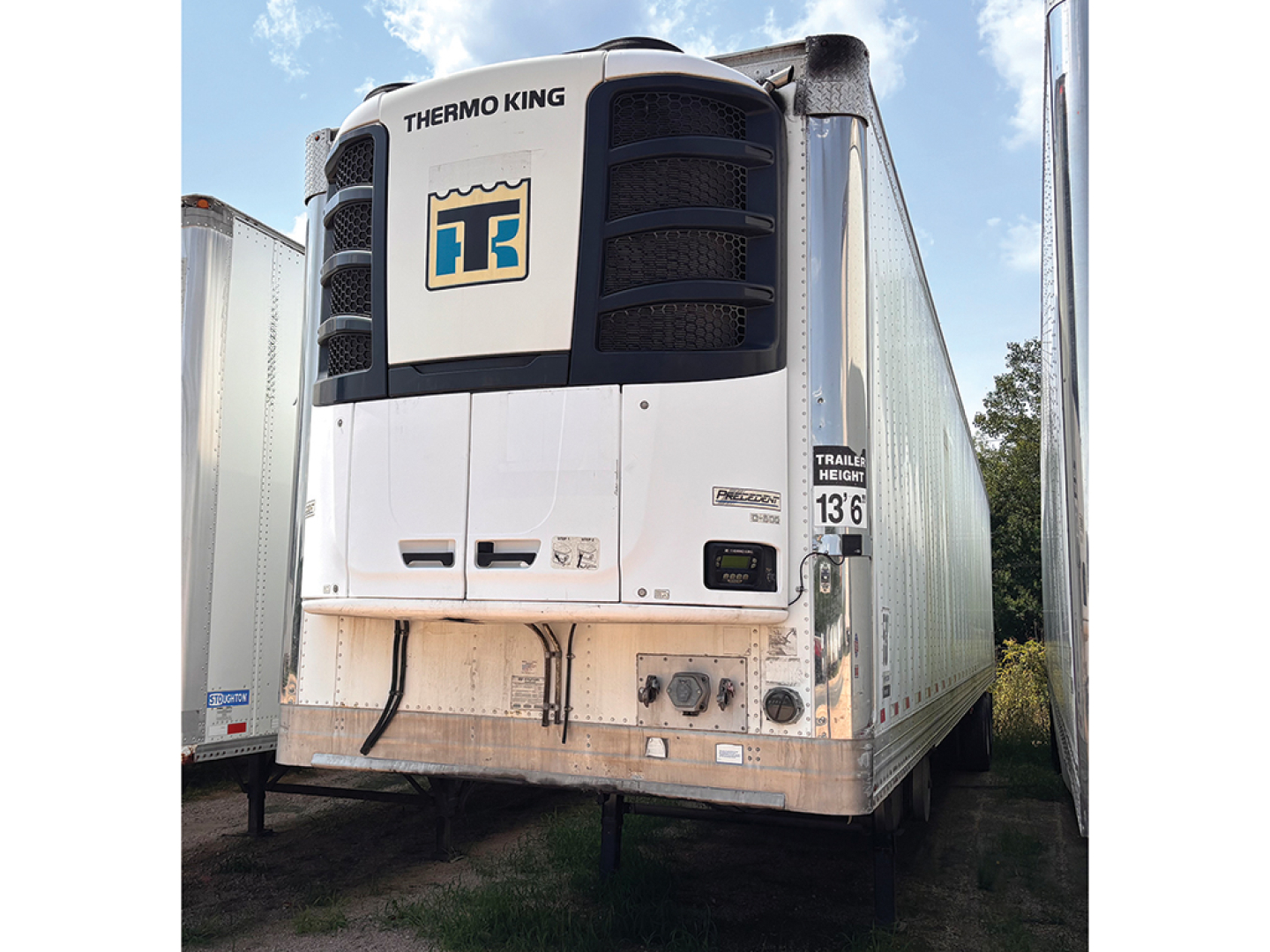 Thermo King reefer trailer nose shows cooling unit and front panel with Thermo King logo; side of trailer visible with weathered white and chrome base.
