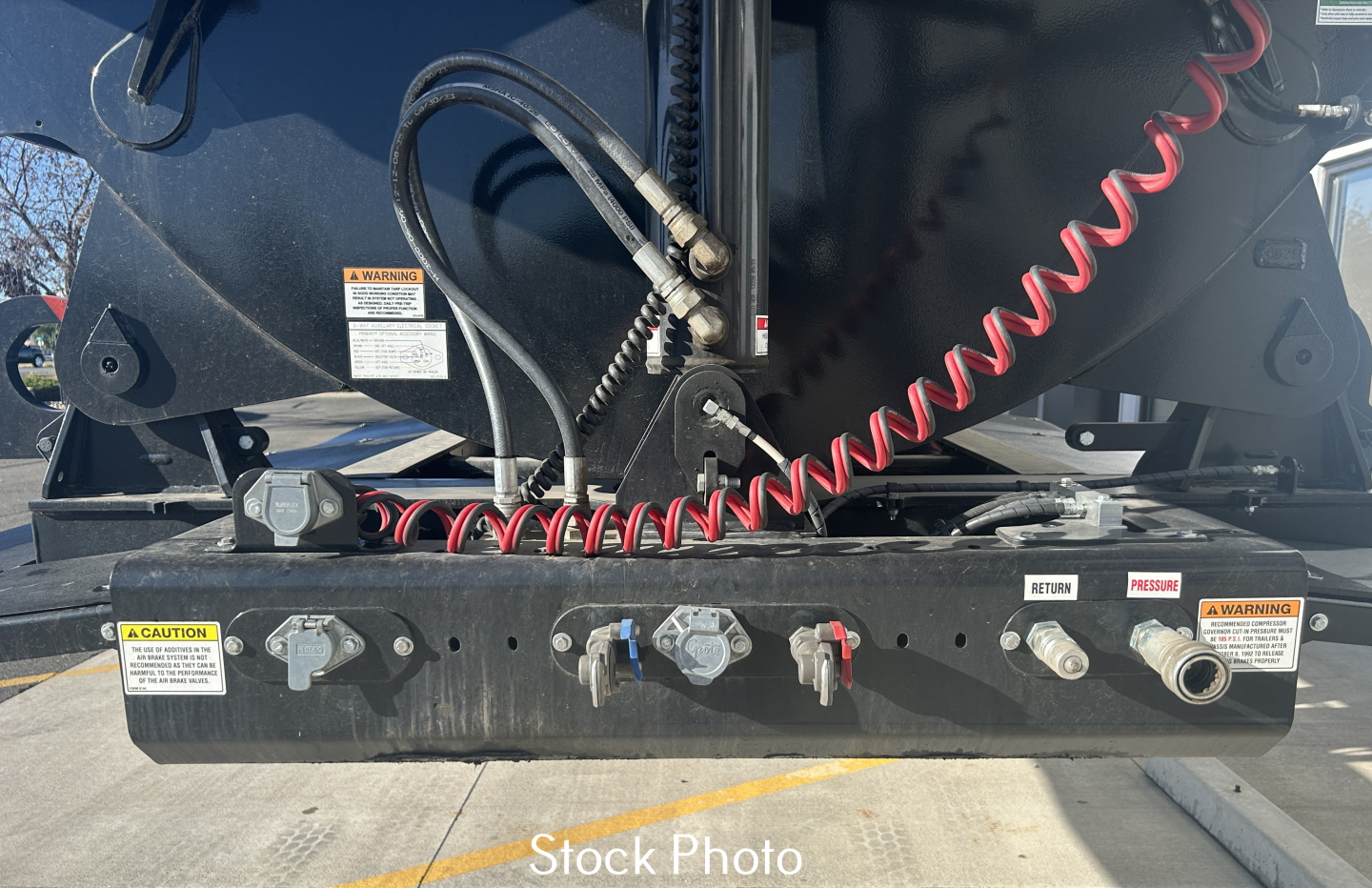 Dump trailer hydraulics and control panel with voltage gauges and warning labels showing coiled red air hose and connectors.