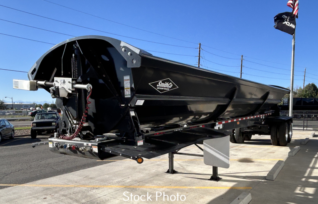 Dump trailer showing Smithco SX2-4034 with black hopper and logo, front hitch, reflective tape, and support legs in a dealership lot.