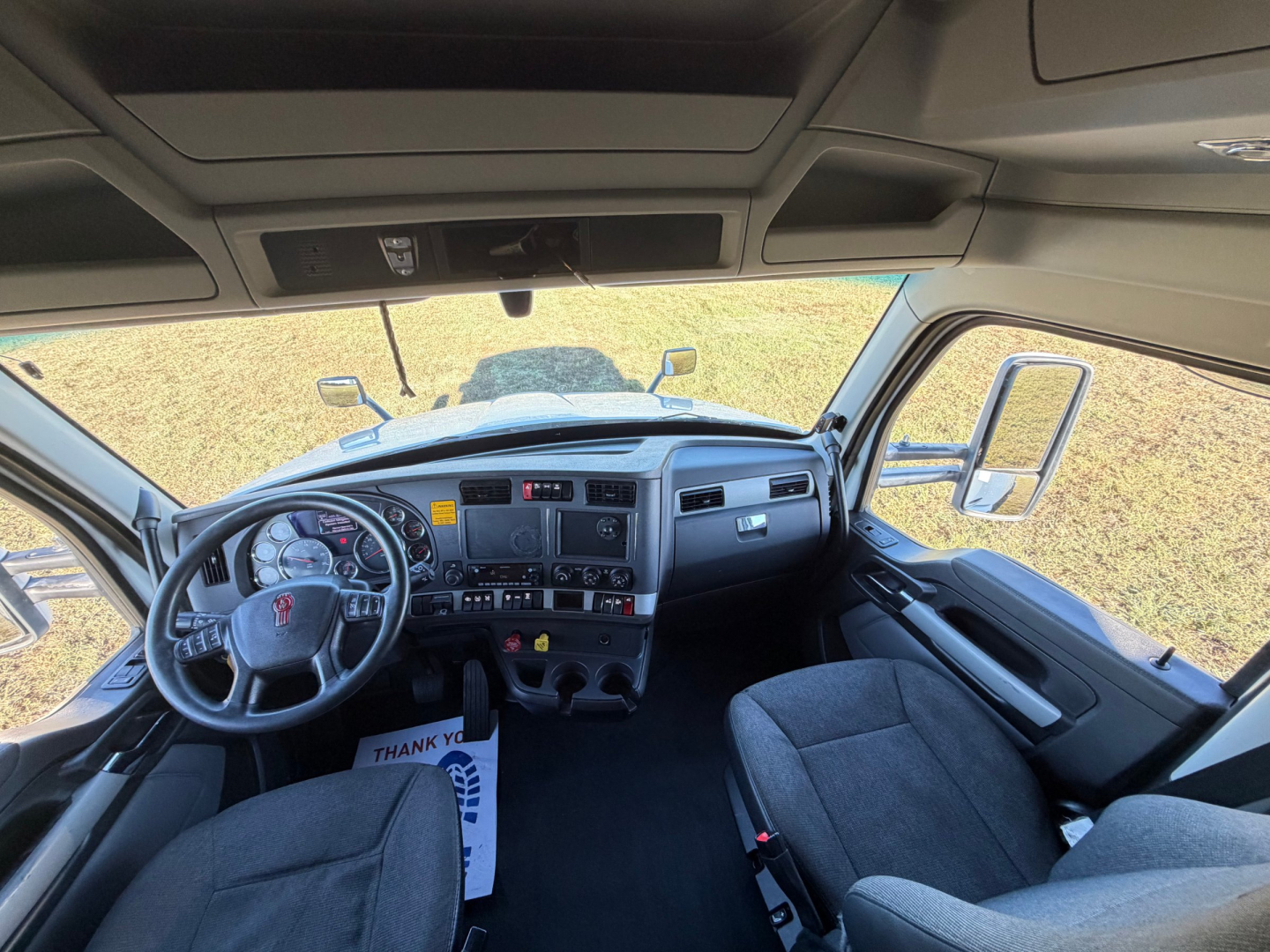 Kenworth T680 interior cab dashboard steering wheel and driver seat with large windshield and side mirrors.