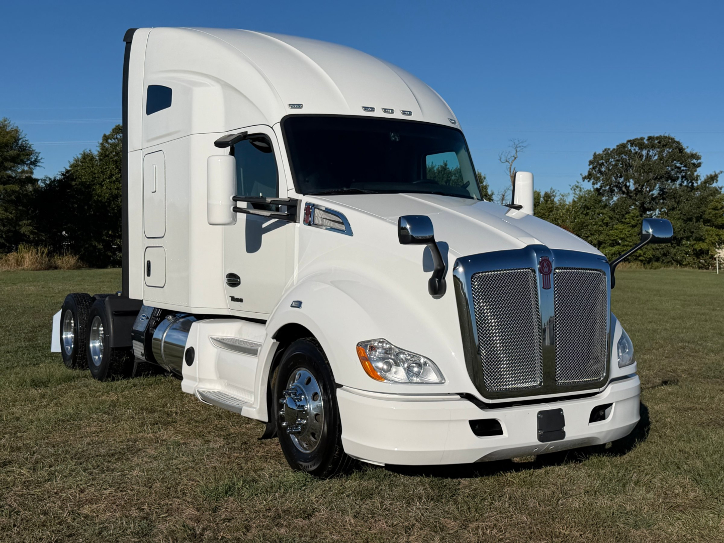 Kenworth T680 conventional sleeper truck with white cab, chrome grille, and dual rear axles; side view showing large mirrors and aerodynamic hood.