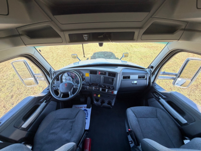 Kenworth T680 cab interior showing steering wheel, dashboard, and two front seats with center console and overhead storage.