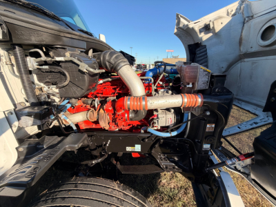 Kenworth T680 engine bay with red engine components and intake hoses visible; tags, hoses, and metal framework in view.