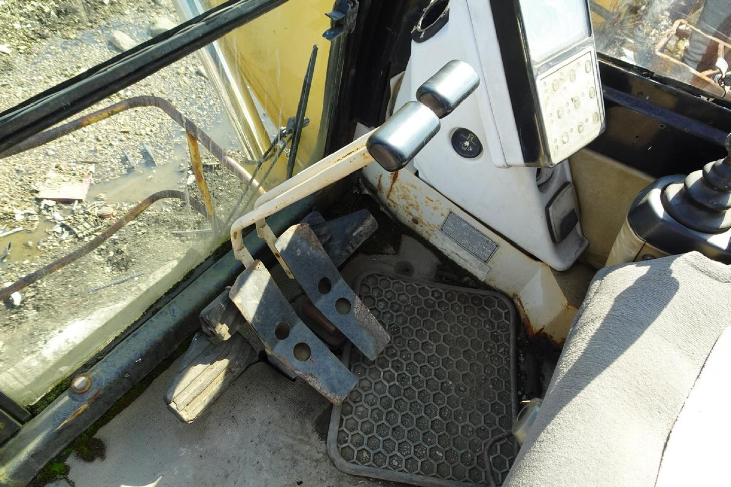 Caterpillar 330L MH cab interior showing foot pedals and service panel; textured rubber floor mat and control levers visible.