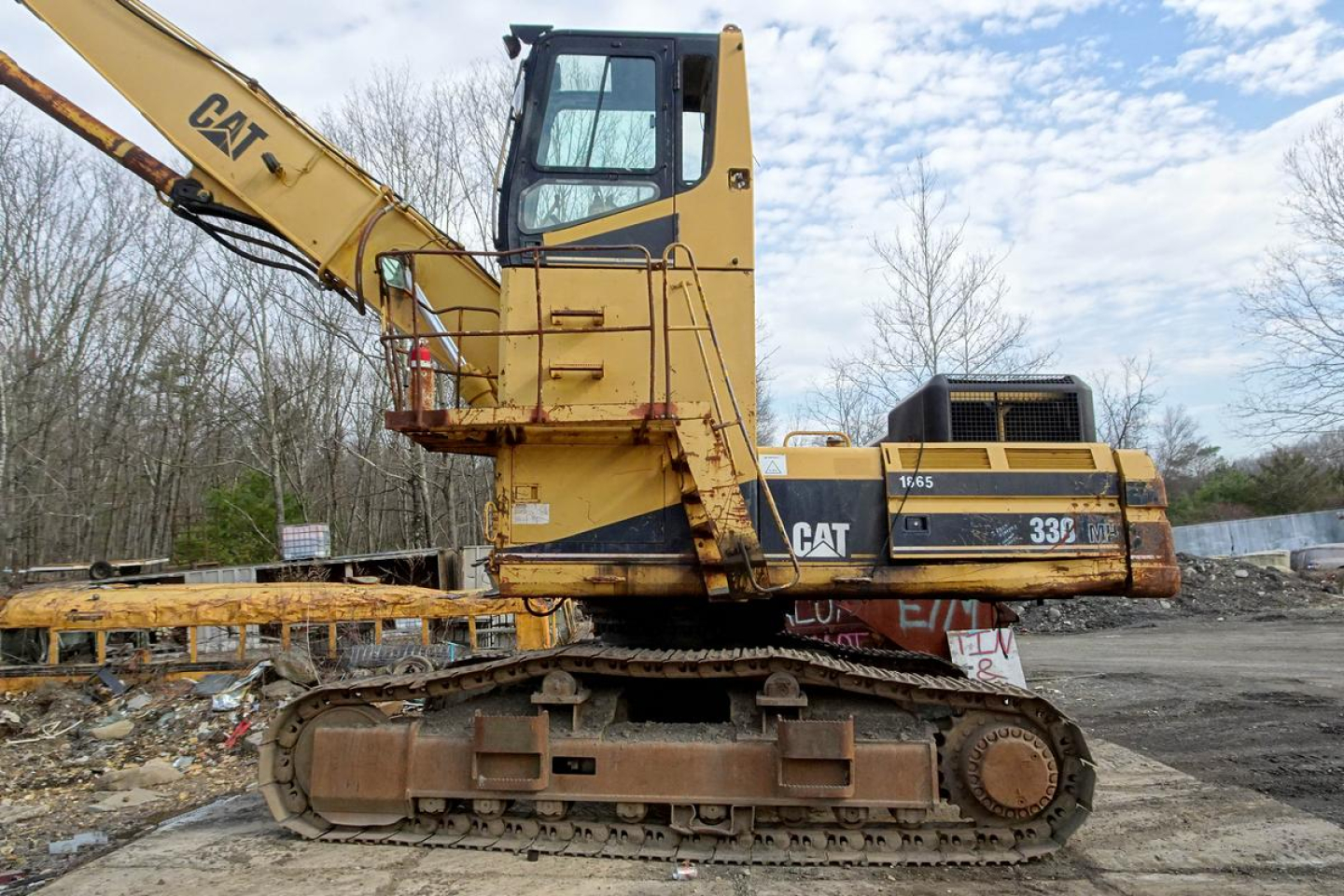 Caterpillar 330L MH excavator in a recycling yard, side view with tracked undercarriage and long boom, yellow paint with CAT branding.