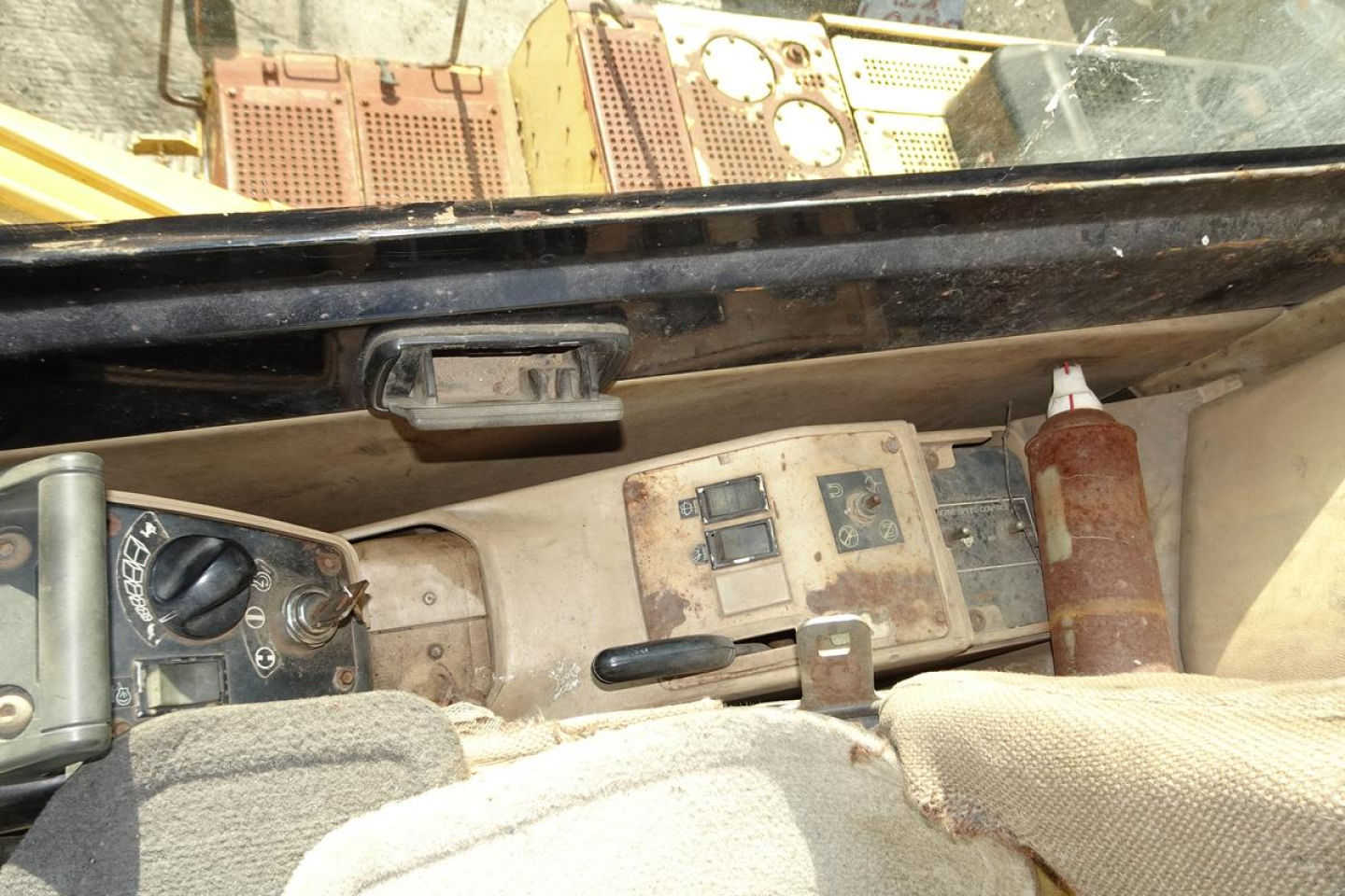 Caterpillar 330L MH truck interior dash area showing switches, ignition, and a brown bottle with nozzle in a dusty cabin.