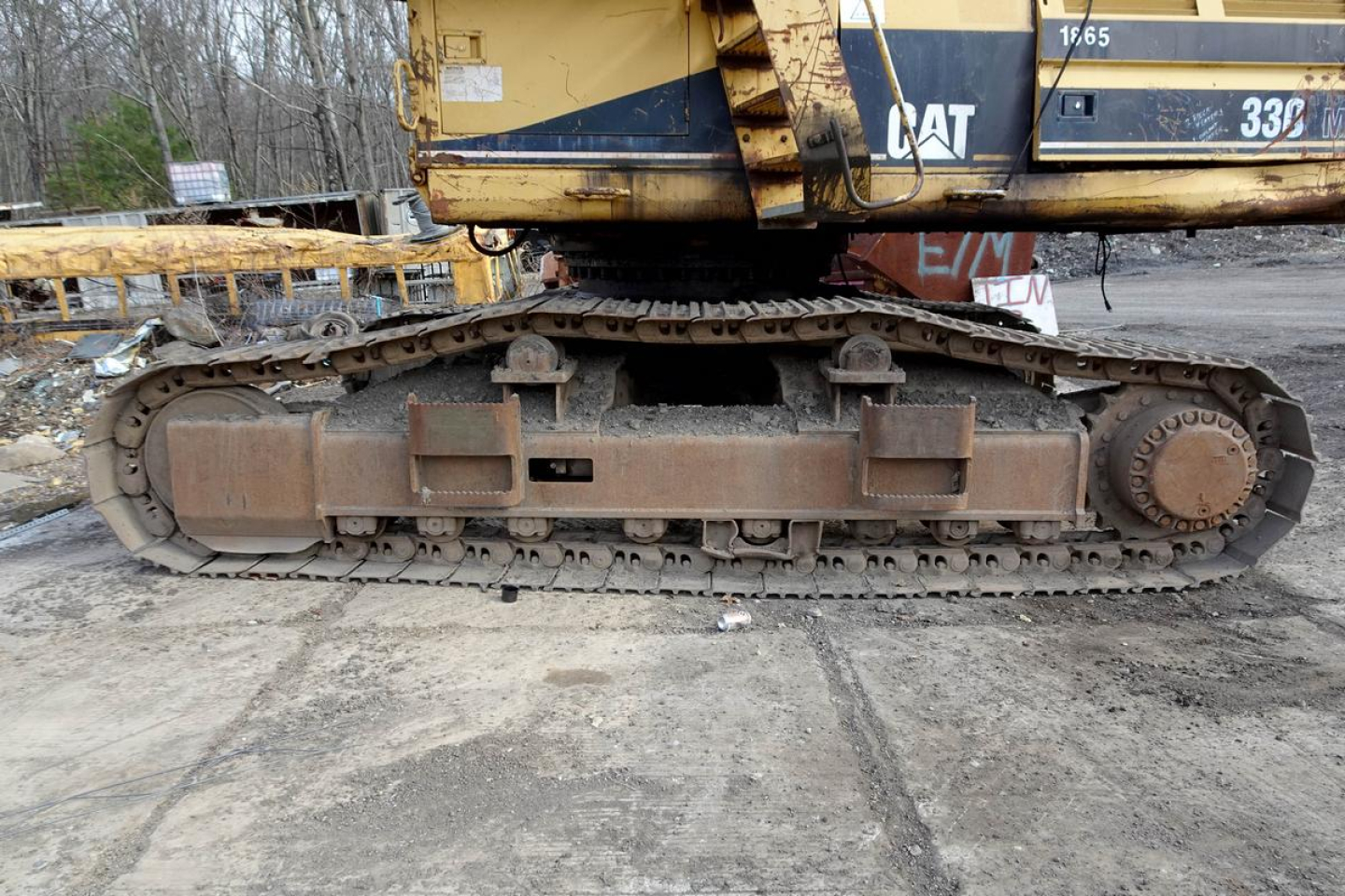 Caterpillar 330L excavator undercarriage with tracked chain and rust-colored metal components in a recycling yard.