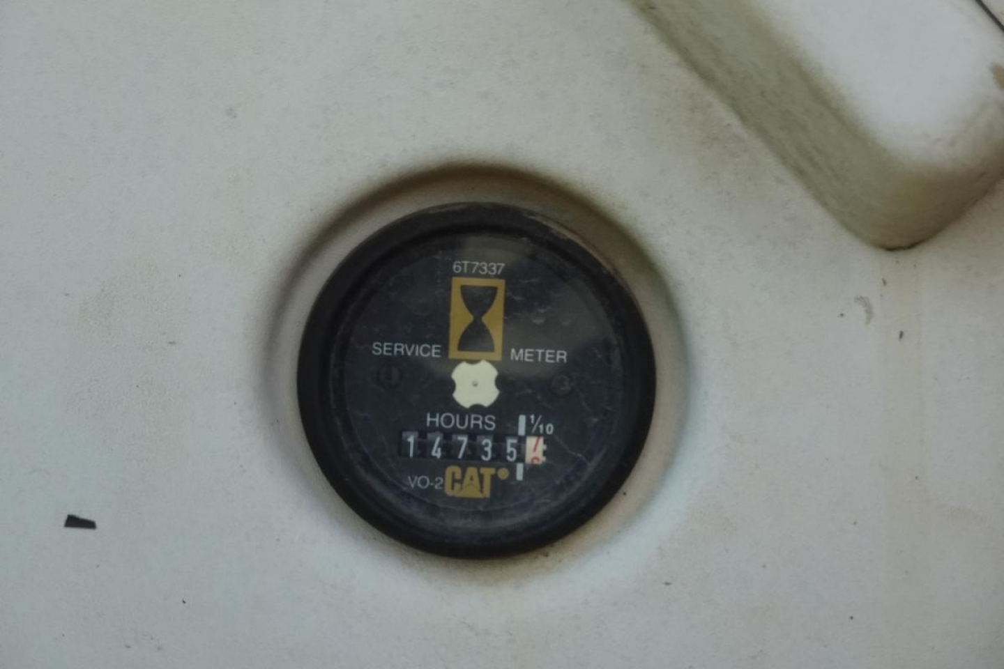 Caterpillar service meter gauge showing hours and CAT logo on a white surface, with numbers 1473.5 and 67633 on dial.