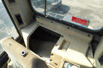 Cab interior of a Caterpillar 330L MH showing dashboard opening with worn beige panels and window with sticker; no specific text legible beyond a small red warning sticker.