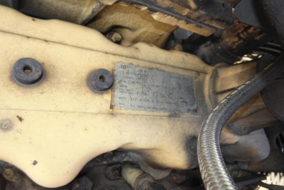 Caterpillar 330L MH engine bay area with nameplate on beige engine block showing serial/part information (blurry plate), hoses and bolts visible.