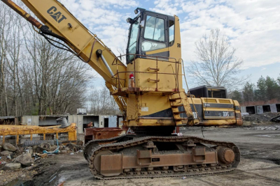 Caterpillar 330L MH excavator in a recycling yard showing operator cab, long arm, and tracked undercarriage.