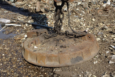 Circular metal Caterpillar 330L MH undercarriage weight plate with chains attached, resting on gravel and debris.
