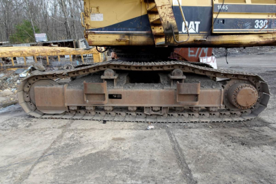 Caterpillar 330L excavator undercarriage with tracked chain and rust-colored metal components in a recycling yard.
