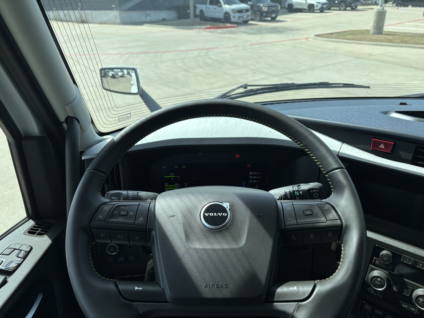 Volvo truck cabin steering wheel and dashboard view in a new 2027 Volvo VNL64T640 sleeper with Volvo emblem on the airbag cover and control buttons on both sides of the wheel.