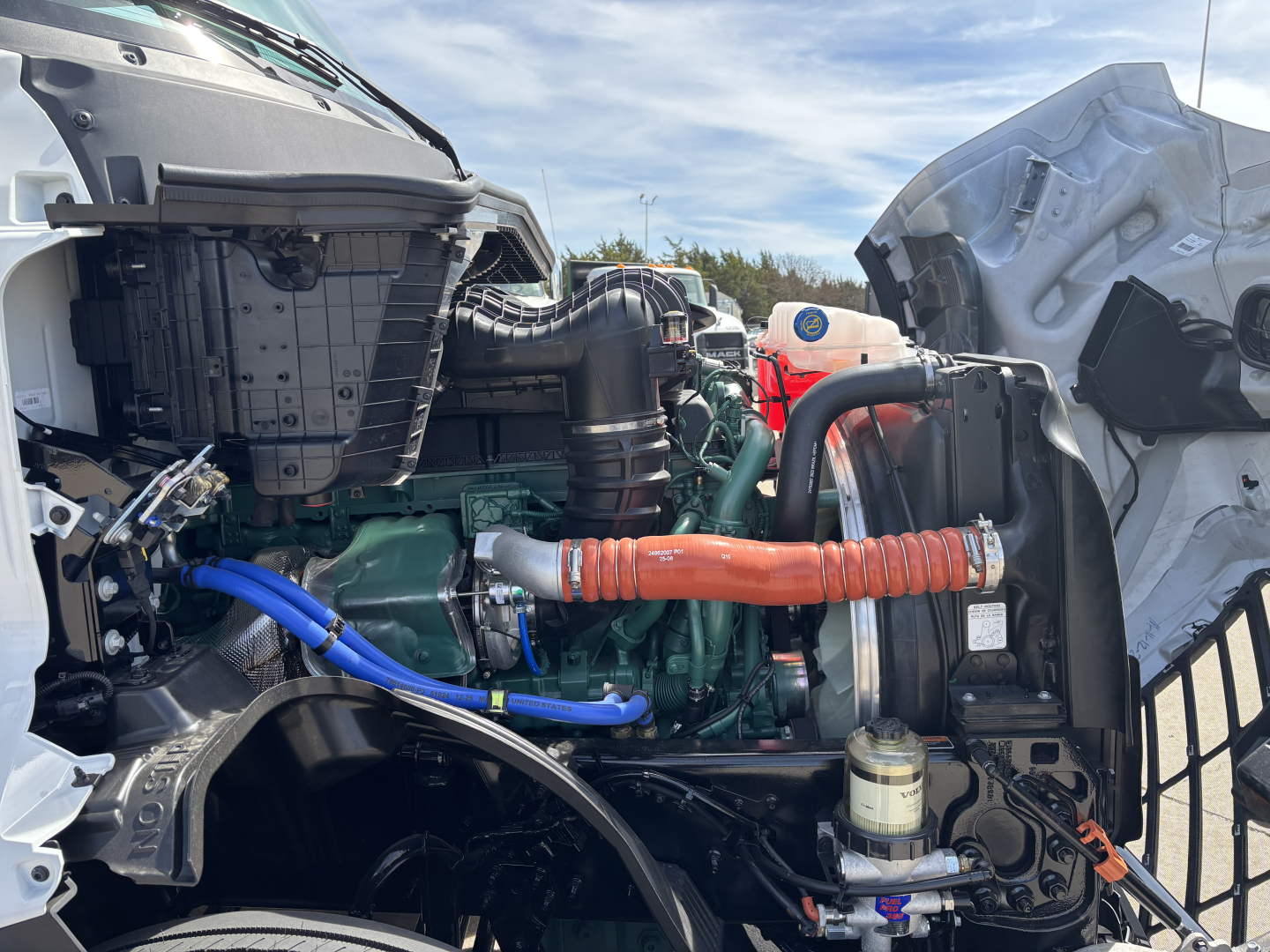 Volvo VNL64T640 engine bay showing green diesel engine, orange insulated hose, blue hose, coolant reservoir, and surrounding components.