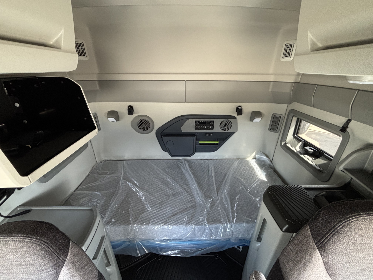 Volvo VNL64T640 sleeper cab interior view with plastic-covered bunk, overhead storage, side window, and control panel on bulkhead.