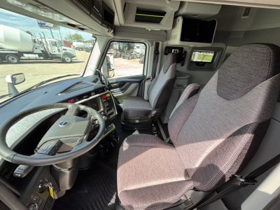 Truck cabin interior showing steering wheel and driver/passenger seats with dashboard controls and overhead cab features.