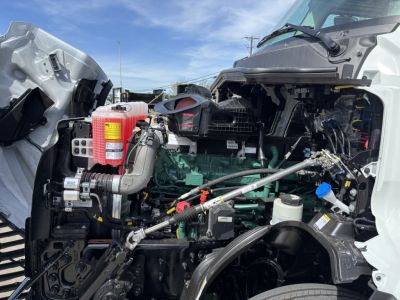 Volvo VNL64T640 engine bay showing green engine block, red fire extinguisher, various hoses and wiring, and visible radiator area.