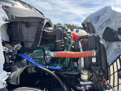 Volvo VNL64T640 engine bay showing green diesel engine, orange insulated hose, blue hose, coolant reservoir, and surrounding components.