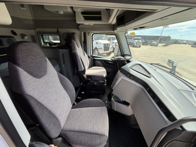 Interior view of a new Volvo VNL64T640 sleeper cab showing driver seat, passenger seat, dashboard, and steering wheel.