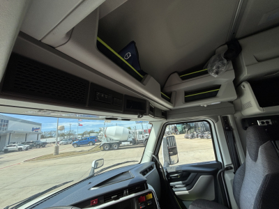  Volvo VNL cab interior showing overhead storage compartments with small labeled items and a sun visor, dashboard, steering wheel, and side window.