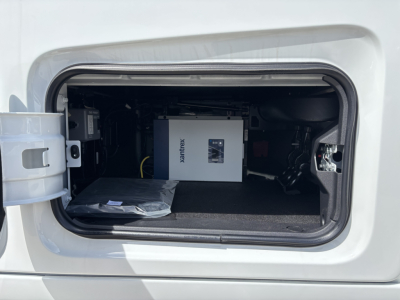 Vehicle storage compartment with Xantrex power inverter visible inside the front bay of a new Volvo VNL64T640 sleeper tractor, cutaway view showing the inverter and cables.