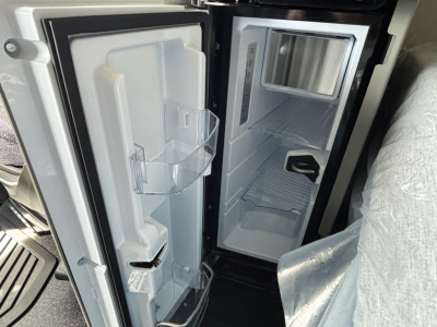 Volvo VNL64T640 sleeper cab interior showing a compact refrigerator/freezer with open doors and shelves.