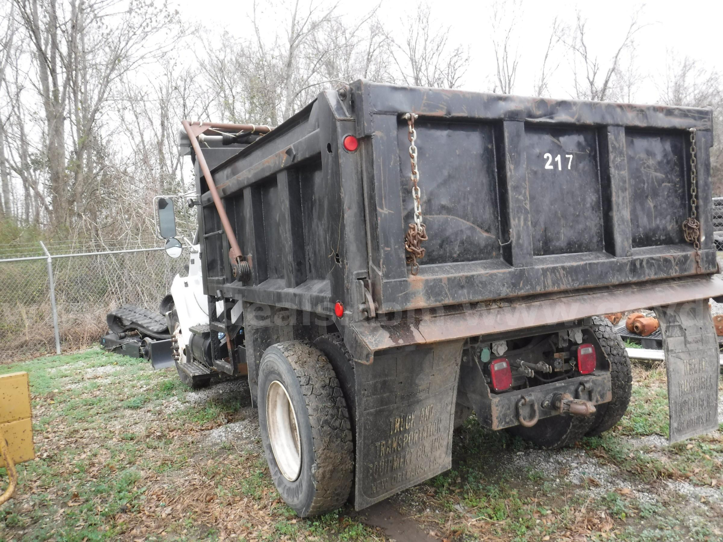 Rear view of a Ford F-750 dump truck with a black dump bed, license-free; visible are large dual rear tires, tailgate chains, rear lights, and a small white cab.
