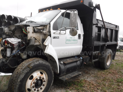 Ford F-750 dump truck with front cab over, hood open showing engine bay, white cab with green decals, black dump bed, spare tires in background.