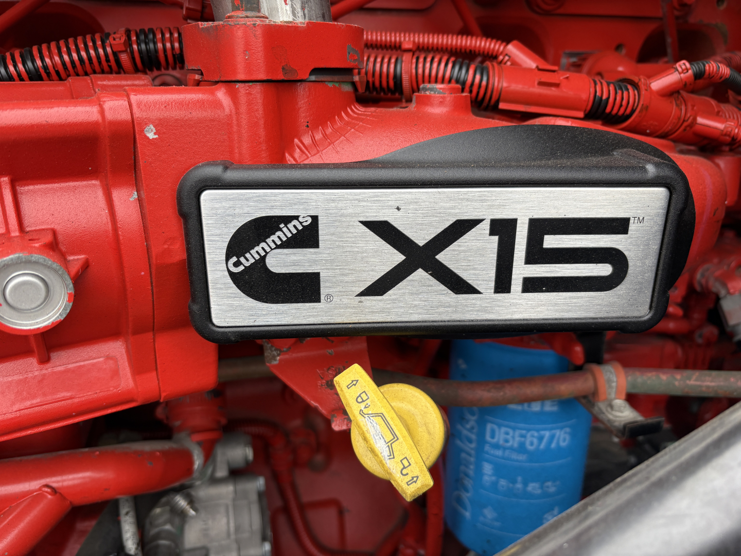 Cummins CX15 engine cover on red International LT625 truck, with yellow dipstick and blue oil filter visible.