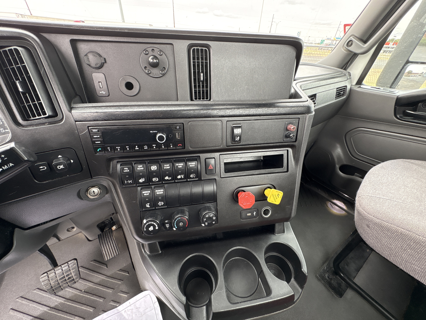 Cab interior of a 2021 International LT625 daycab showing dashboard controls, steering area, and center console with climate controls, radio, a storage tray, and cup holders.
