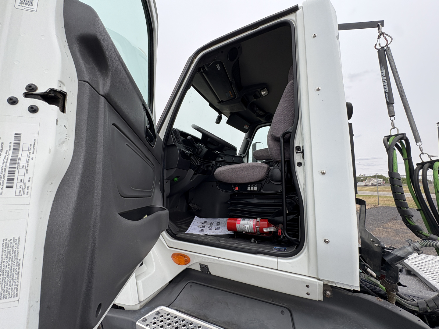 Truck cab interior of a 2021 International LT625 Daycab, driver seat and dashboard visible through open door, VIN 3HSDZAPR7MN607115, stock B3182P, exhaust and controls present.