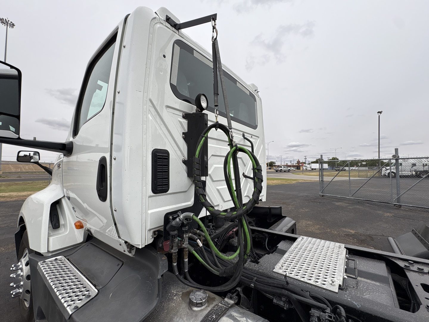 Truck cab of a 2021 International LT625 conventional daycab, side view showing roof-mounted mirrors, rear cab area with green hoses, metal diamond-plate steps, and hitch area.