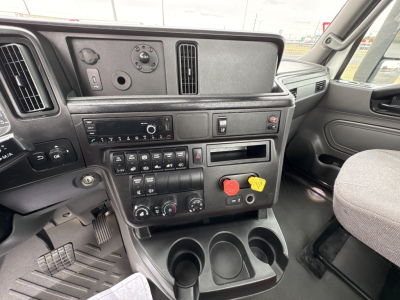 Cab interior of a 2021 International LT625 daycab showing dashboard controls, steering area, and center console with climate controls, radio, a storage tray, and cup holders.