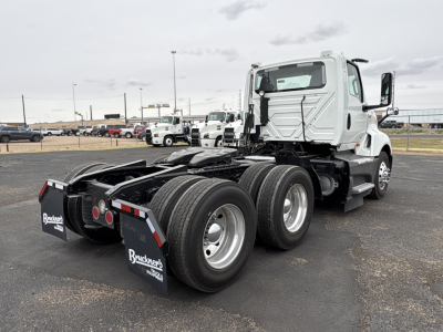 Truck rear/side view showing chassis and dual rear axles, with mudflaps labeled Buuckney? Buckneck? hardware. Visible text on mudflaps: Brackets? The image includes a white International LT625 daycab tractor in a lot.