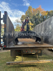 Truck bed with grapple loading tool on a flatbed, viewing rear with forked grapple attachment and hydraulic arm.