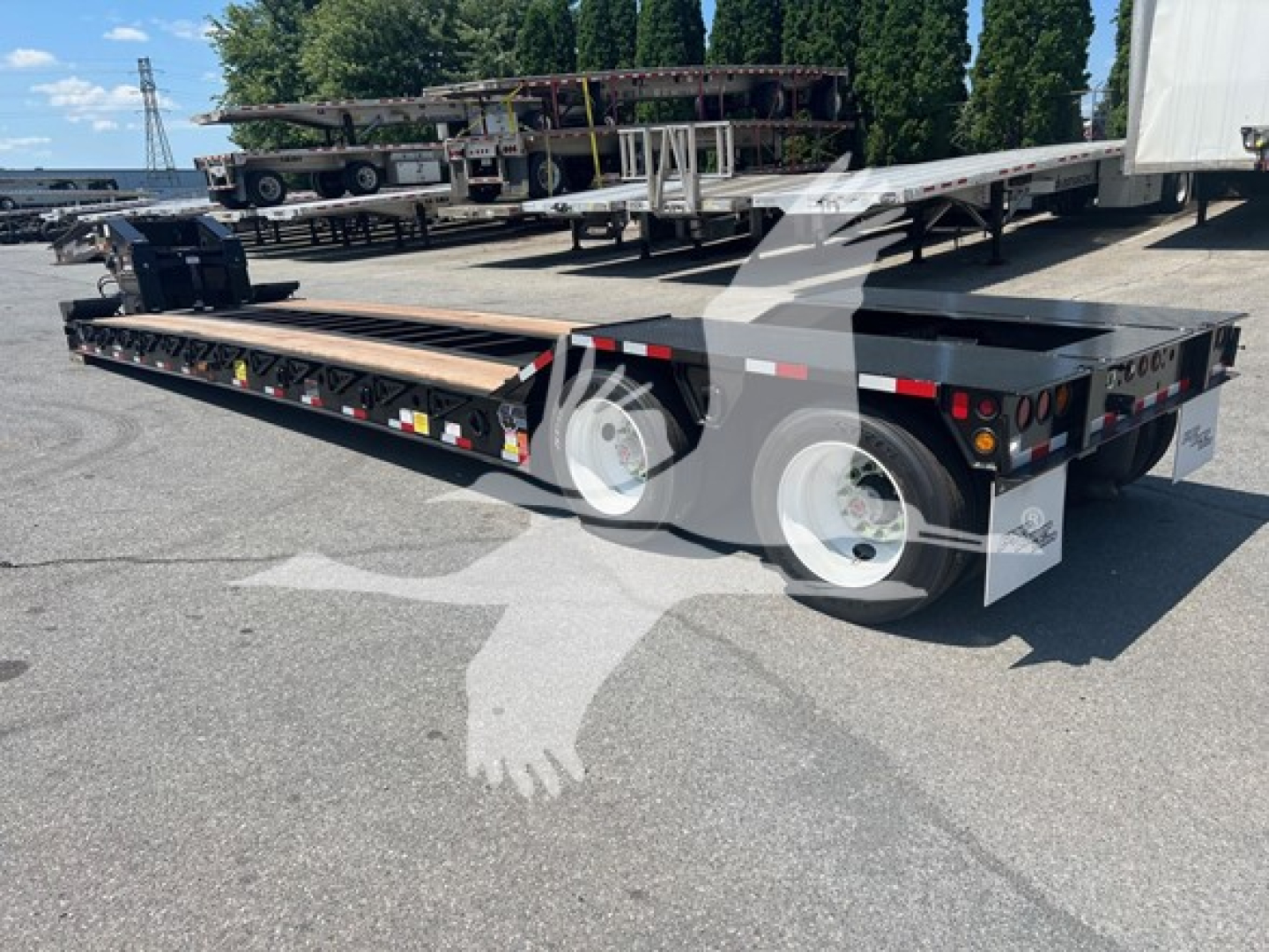 Trailer with flatbed lowboy, dual rear axles, and white wheels. Visible decals and taillights on rear deck; long metal frame with side reflectors.