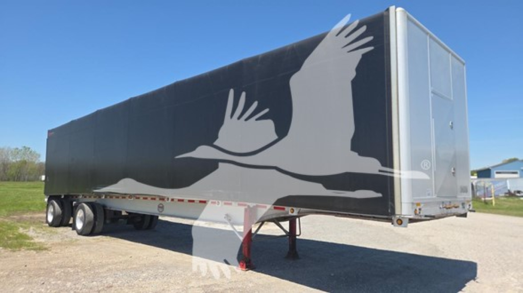 Curtainside trailer showing graphic of flying cranes on black sides and rear doors open, Mac Aluminum 2013 model in a yard.