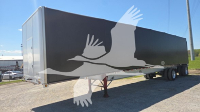 Curtainside trailer in view showing black and gray exterior with graphic camo-like design and dual rear wheels.