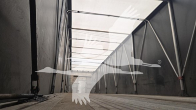 Trailer interior showing open side curtain area with framework and aisle, scuffed floor, light entering from roof; no legible labels visible.