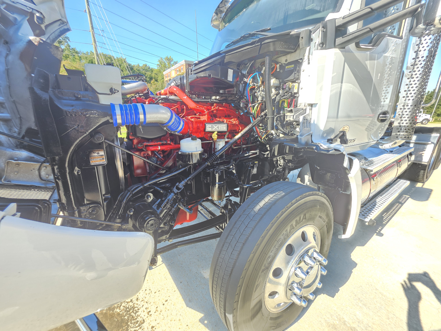 Kenworth T880 conventional daycab truck with open hood showing red engine components and blue hoses; front right wheel visible; partial side view of cab and chassis.